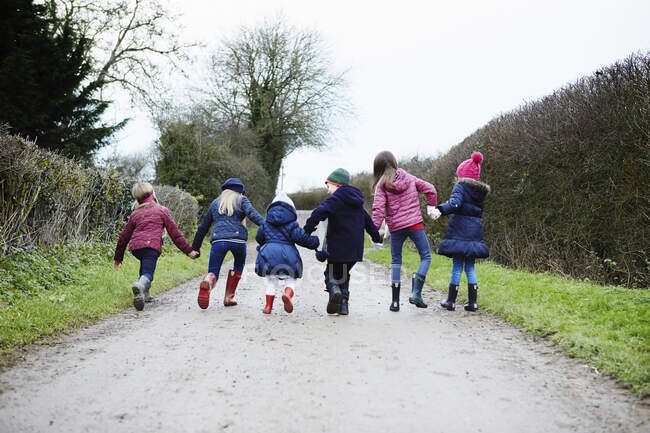 Rear view of boy and girls holding hands and fooling around on rural road — Stock Photo