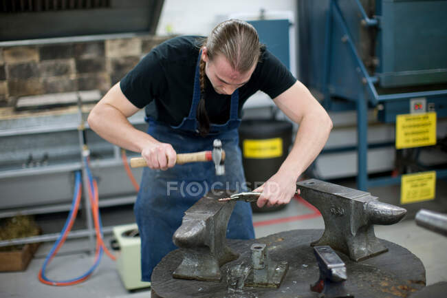 Чоловік використовує молоток для металообробки в творчій студії — стокове фото