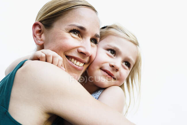 Retrato de mujer adulta mediana y su hija abrazándose frente a la pared blanca - foto de stock