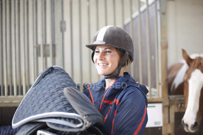 Молода жінка тримає конячу ковдру і сідло — стокове фото