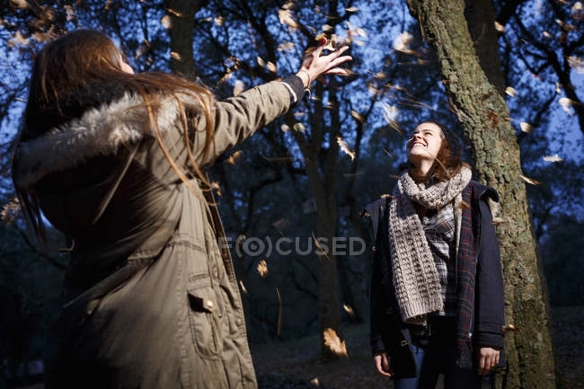 Sisters scattering leaves into air in autumnal forest — Stock Photo
