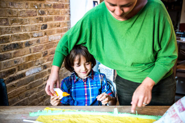 Мама помогает сыну намазывать клей на блинную бумагу, чтобы сделать пиньяту. — стоковое фото