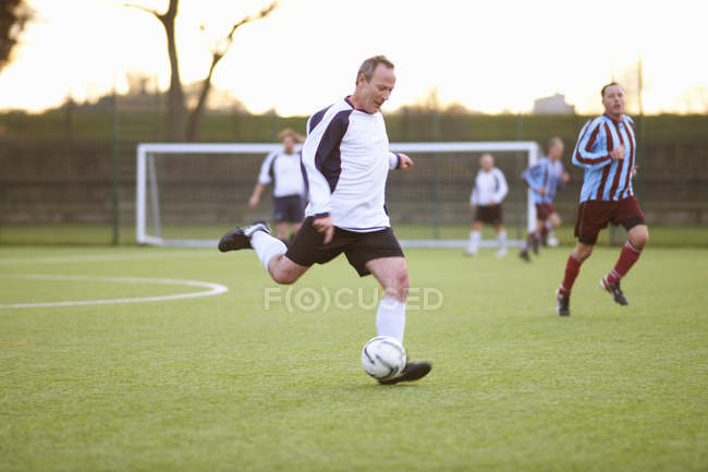Футболист пинает мяч на поле — стоковое фото