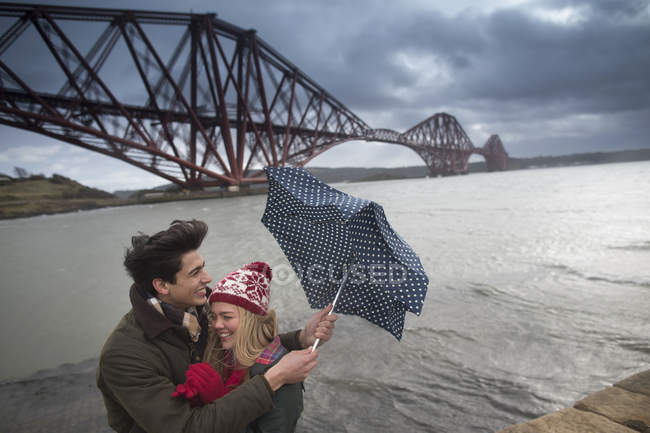 Una joven pareja posa frente al Forth Rail Bridge en Queensferry, cerca de Edimburgo, Escocia - foto de stock