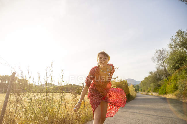 Счастливая молодая женщина в красном платье, бегущая по сельской дороге, Майя, Испания — стоковое фото