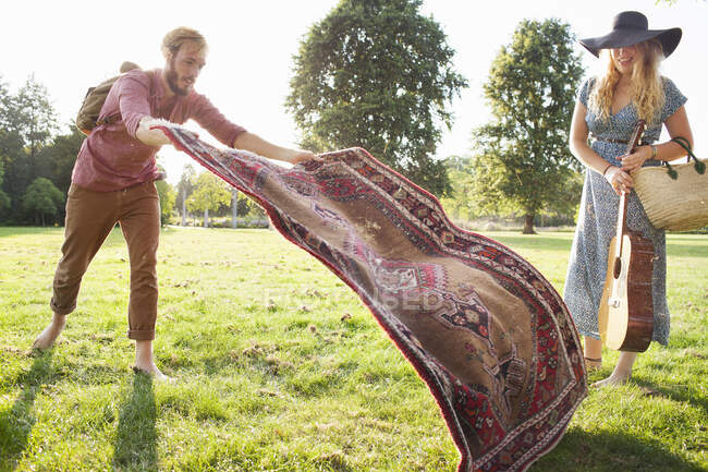Romântico jovem casal espalhando tapete para piquenique no parque — Fotografia de Stock