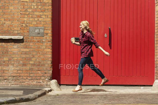 Mujer caminando por la puerta roja, Londres, Reino Unido - foto de stock
