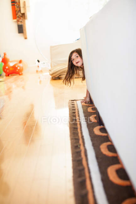 Girl peering from behind sofa, portrait — Stock Photo