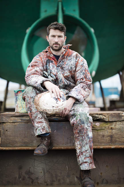 Portrait of male ship painter sitting in front of green ship hull — Stock Photo