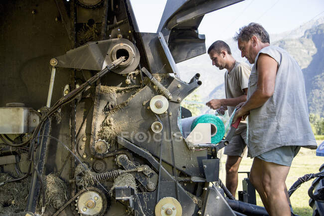 Two male farmworkers untangling netting in hay baler — Stock Photo