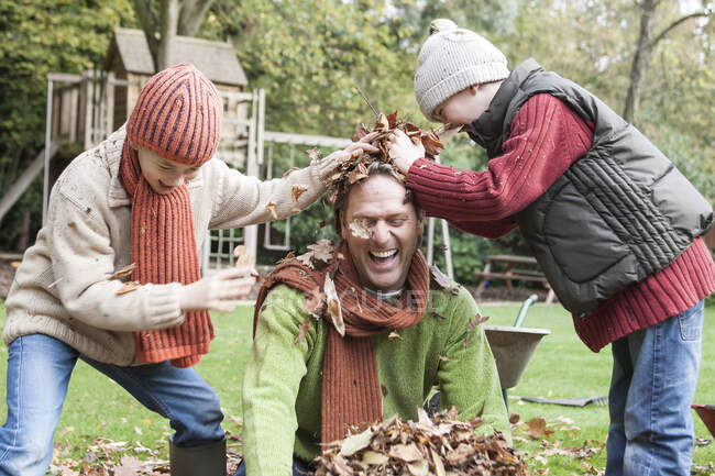 Батько і сини дуріють в саду, кидаючи осіннє листя. — стокове фото
