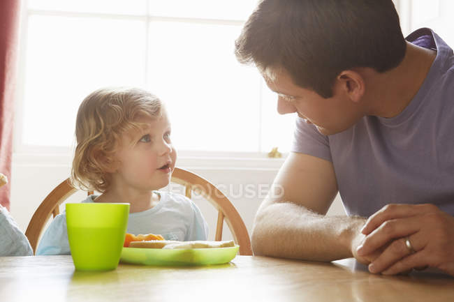 Hombre adulto medio y su hija pequeña en la mesa de la cocina - foto de stock