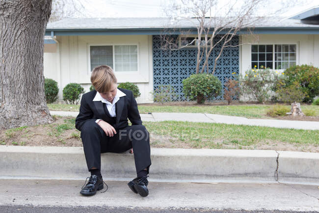 Menino de terno sentado na rua suburbana — Fotografia de Stock