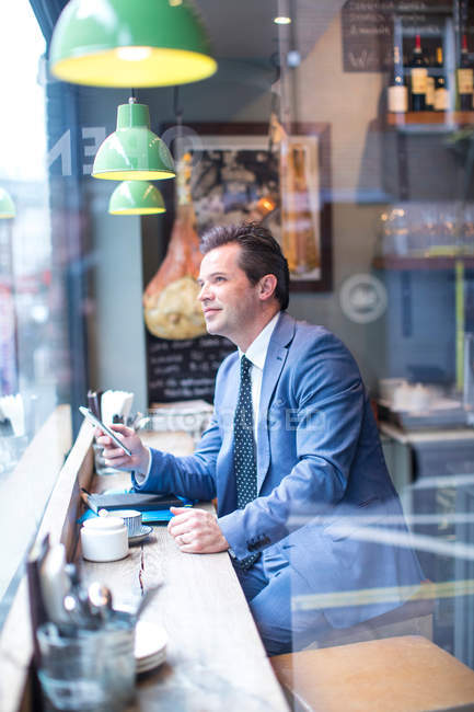 Uomo d'affari maturo con smartphone nel finestrino del ristorante — Foto stock