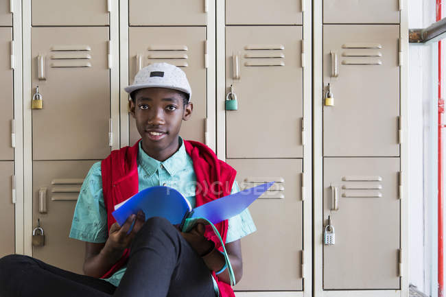 Student leaning against lockers, looking up from textbook — Stock Photo