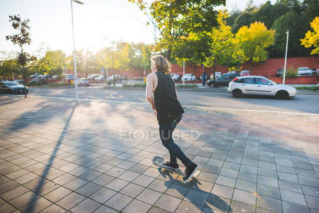 Молодой городской скейтбордист катается на скейтборде вдоль тротуара — стоковое фото