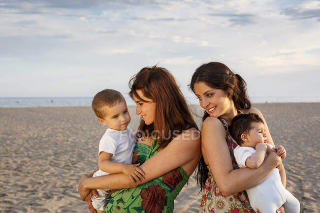 Mães em pé na praia segurando bebê e criança — Fotografia de Stock