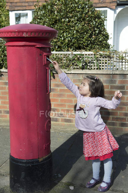 Young girl at post box, reaching up to post letter — Stock Photo