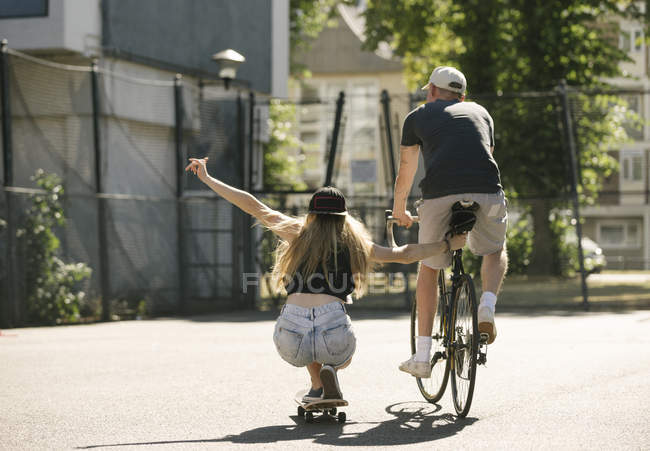 Вид сзади женщины-скейтбордиста и велосипедиста-мужчины на баскетбольной площадке — стоковое фото