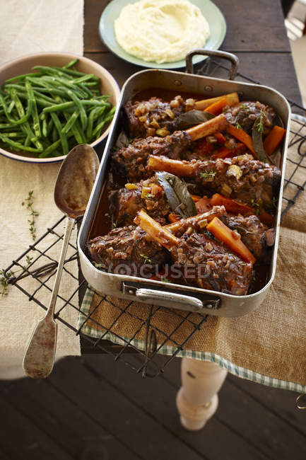 Top view of lamb shank stew in roasting tin with green beans and mashed potatoes — Stock Photo