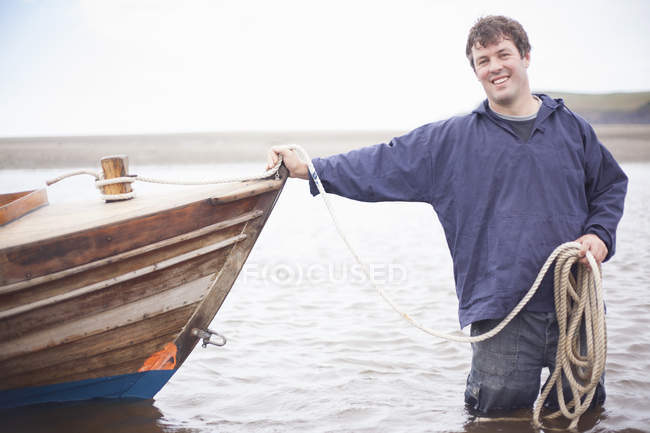 Portrait of man holding rope and leaning on rowing boat — Stock Photo