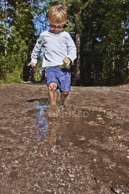 Маленький мальчик брызгает в грязную лужу — стоковое фото