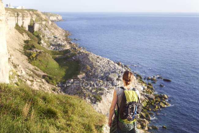 Вид сзади женщины с рюкзаком, смотрящей на океан, Портленд, Великобритания — стоковое фото