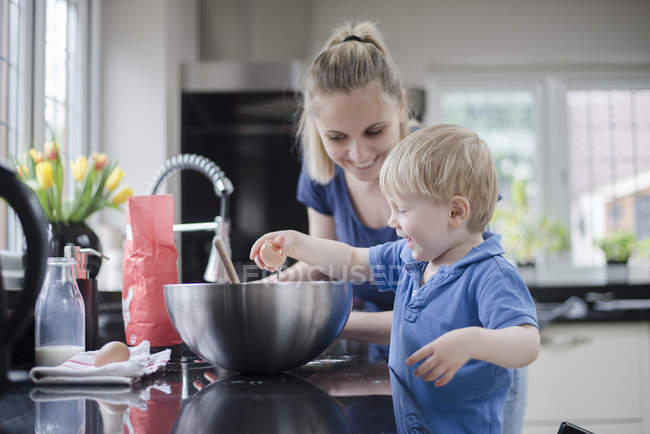 Mãe ajudando filho assar bolo, filho rachando ovo — Fotografia de Stock