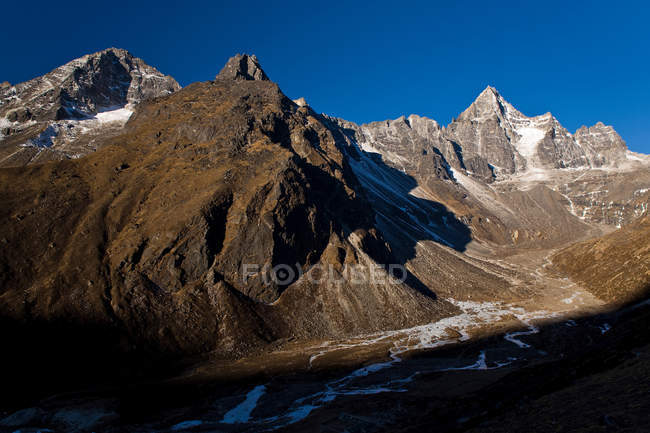 Montanhas rochosas cobertas de neve e vale em luz solar brilhante — Fotografia de Stock