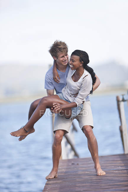 Young couple on jetty, cheerful man lifting woman — Stock Photo