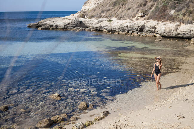 Giovane donna in costume da bagno chatta su smartphone in spiaggia, Villasimius, Sardegna, Italia — Foto stock