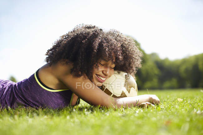 Молодая женщина отдыхает в парке, опираясь на футбол — стоковое фото