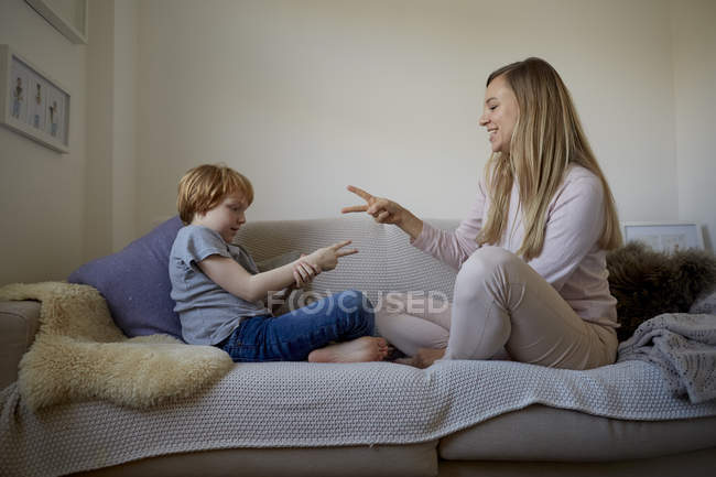 Середня доросла жінка і син грають рок-паперові ножиці на дивані — стокове фото