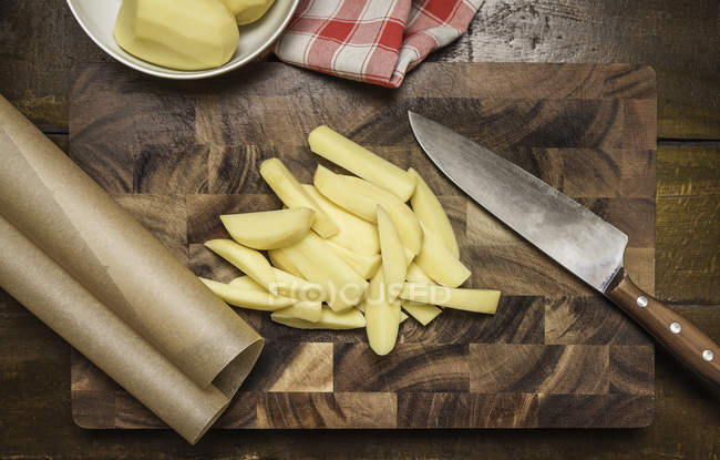 Vista superior de batatas descascadas e fatiadas, faca de cozinha na tábua de corte — Fotografia de Stock