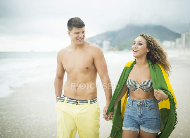 Junges paar spazieren, frau in brasilianische fahne gehüllt, ipanema beach, rio de janeiro, brasilien — Stockfoto