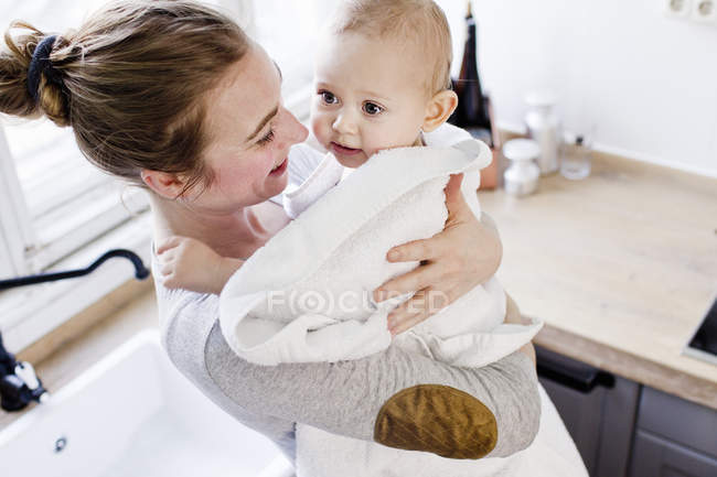 Mère portant bébé fils enveloppé dans une serviette — Photo de stock
