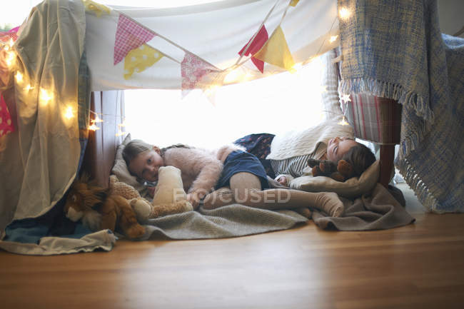 Dos hermanas en la guarida del dormitorio acostadas con juguetes suaves - foto de stock