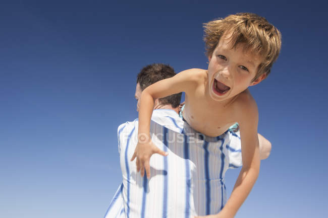 Мальчика везут через плечо отцов на голубое небо — стоковое фото