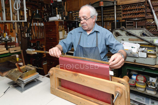 Hombre mayor que mide la columna vertebral del libro en el taller tradicional de encuadernación - foto de stock