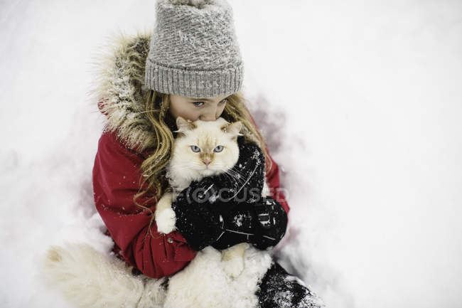 Porträt einer weißen Katze mit grünen Augen, die von einem Mädchen im Schnee umarmt wird — Stockfoto