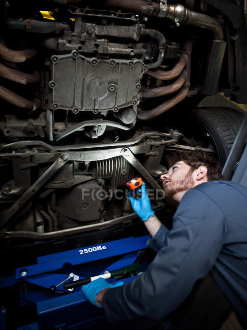 Mechaniker hält Taschenlampe in der Hand, schaut unter Auto — Stockfoto