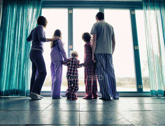 Family in pajamas looking out window — Stock Photo