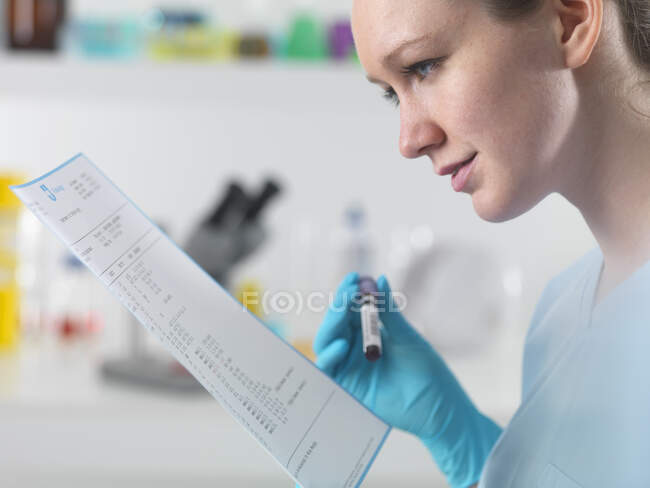 Técnico que sostiene la muestra de sangre en el laboratorio clínico con los resultados de la prueba - foto de stock
