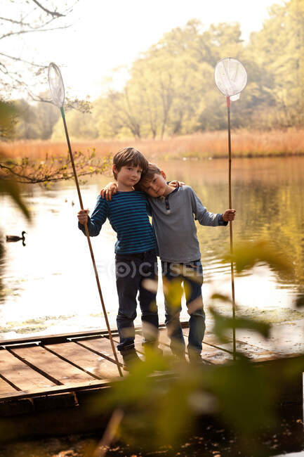 Hermanos de pie juntos en el muelle sosteniendo redes de pesca, retrato - foto de stock