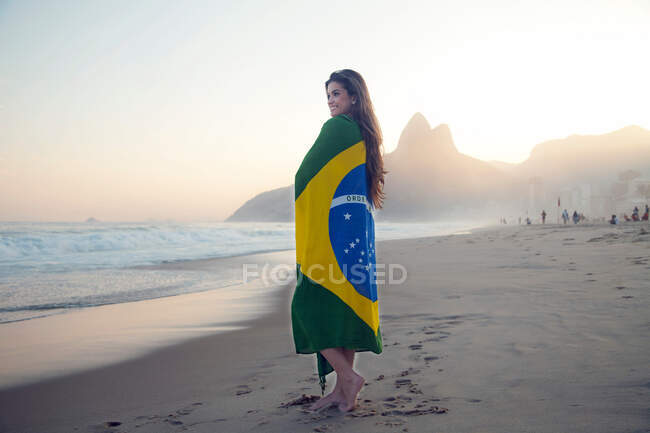 Young woman on beach, wrapped in Brazilian Flag — Stock Photo