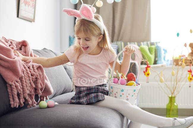Girl finding easter eggs under sofa blanket — Stock Photo