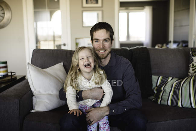 Retrato de homem sentado no sofá com a filha no joelho — Fotografia de Stock