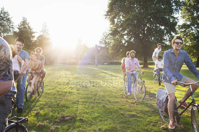 Rangées de fête allant adultes arrivant dans le parc sur les vélos au coucher du soleil — Photo de stock