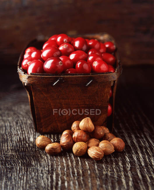 Food, rustic punnet full of cranberries and hazelnuts, wooden table — Stock Photo