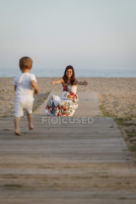 Niño corriendo hacia la madre en el paseo marítimo - foto de stock